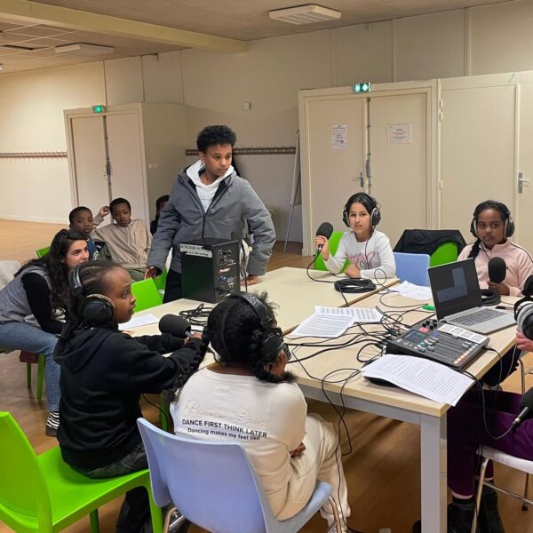 Quatre enfants sont autour d'une table, casque sur les oreilles et micro à la main, en train d'enregistrer une émission de radio.