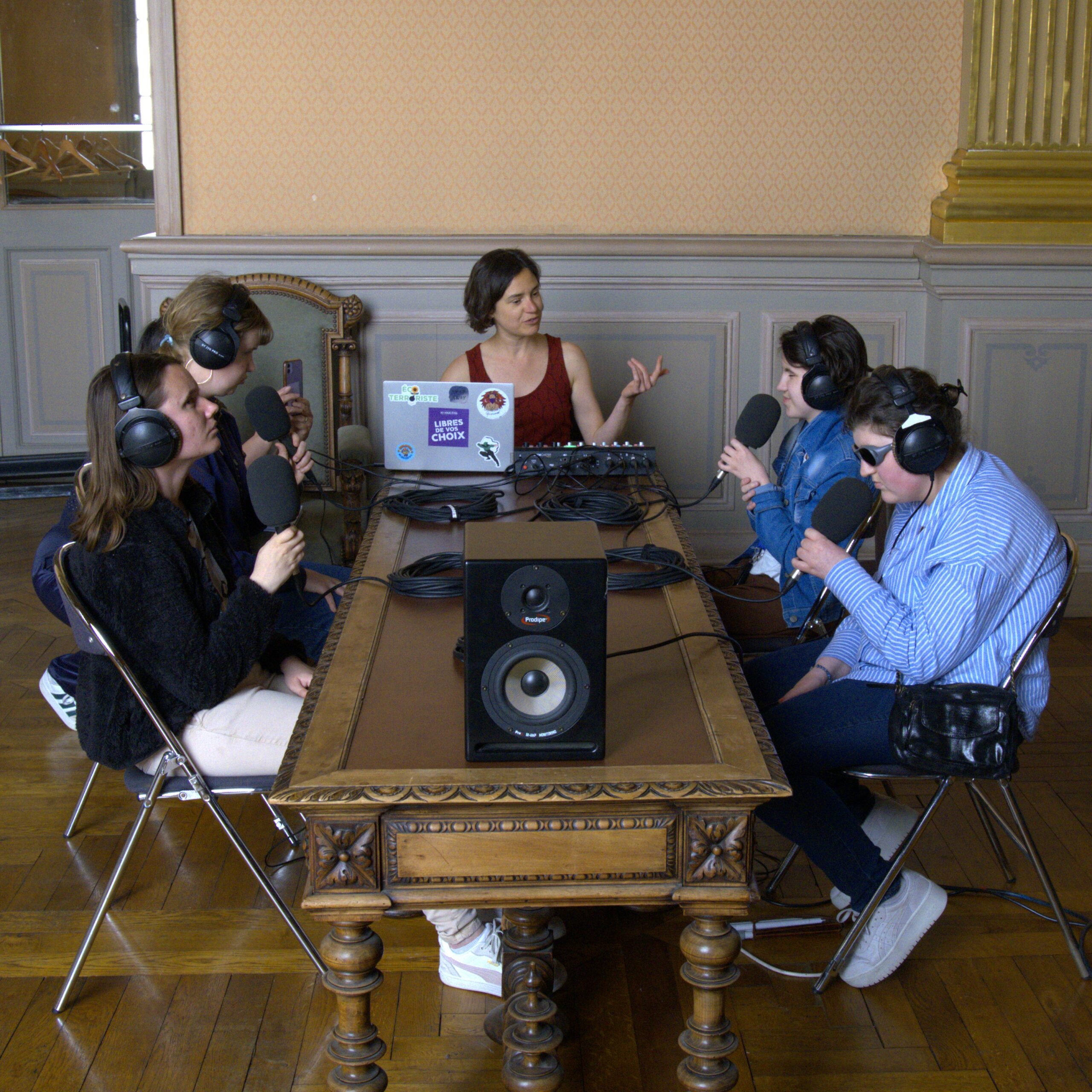 Quatre jeunes femmes déficientes visuelles sont assises autour d'une longue table en bois sculpté, casque sur les oreilles, micro à la main, en train d'enregistrer une émission de radio dans le foyer du Grand-Théâtre d'Angers.